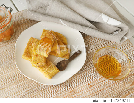 Slices of fried hard polenta with honey on plate on table. Cornmeal in kitchen. Ingredients and traditional Italian cuisine. 137249711