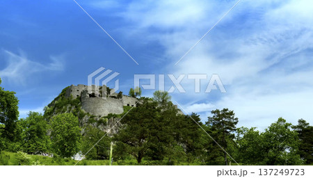 Visitors explore the ancient castle on a hill surrounded by green trees under a clear blue sky in springtime Visitors explore the ancient castle on a hill surrounded by green trees under a clear blue sky in springtime 137249723