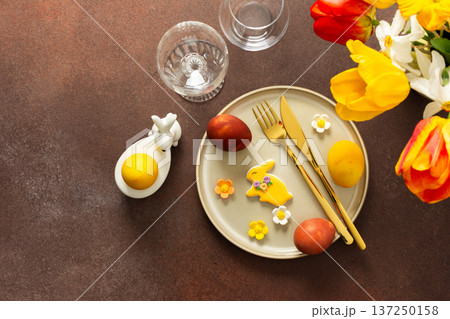 A beautifully arranged Easter table displays vibrant eggs, elegant gold cutlery, and a lively bouquet of tulips and lilies. This setting creates a cheerful atmosphere for the holiday feast 137250158