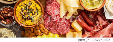A colorful charcuterie board offers an inviting selection of cheeses, cured meats, fresh bread, nuts, and creamy hummus, perfect for sharing at a casual gathering or picnic, banner 137250702