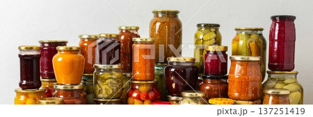 Canned vegetables and fruits are stacked on a shelf, prepared for winter use. Various jars hold different preserves, showcasing careful efforts for storing food during the season, banner 137251419