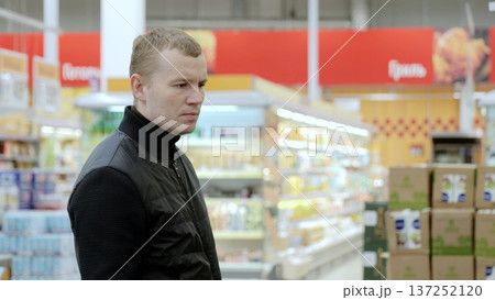 Focused man choosing food in supermarket aisle, emphasizing healthy eating and nutrition in lifestyle. A man studies the label on a bottle of sauce Focused man choosing food in supermarket aisle, emphasizing healthy eating and nutrition in lifestyle. A man studies the label on a bottle of sauce 137252120