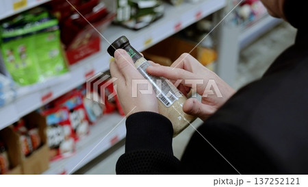 Customer is reading the nutritional information and ingredients on a bottle of dressing while shopping in a grocery store. A customer in black studies the label on a bottle of sauce 137252121