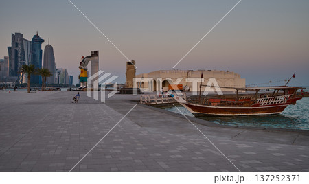 Doha Qatar skyline from corniche promenade sunset shot showing dhows in Arabic gulf with Qatar flag Doha Qatar skyline from corniche promenade sunset shot showing dhows in Arabic gulf with Qatar flag 137252371