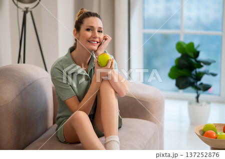 Pretty young woman in green home wear with apple in hands Pretty young woman in green home wear with apple in hands 137252876