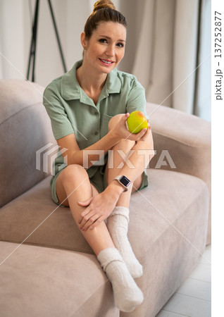 Pretty young woman in green home wear with apple in hands Pretty young woman in green home wear with apple in hands 137252877