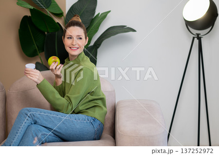 Young smiling woman in green with apple in hand Young smiling woman in green with apple in hand 137252972
