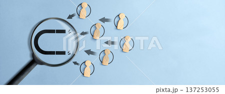Top view of wooden figures being drawn by a magnet icon through a magnifying glass on a light blue background. Illustrates lead generation, HR recruitment, and client acquisition concepts 137253055