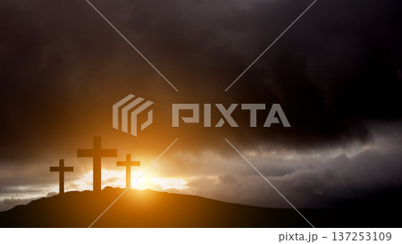 Silhouette of three wooden crosses standing on a hilltop under a dark, stormy, and dramatic sky with golden sunlight breaking through the clouds. Symbolic of Calvary, Easter, and religious faith 137253109