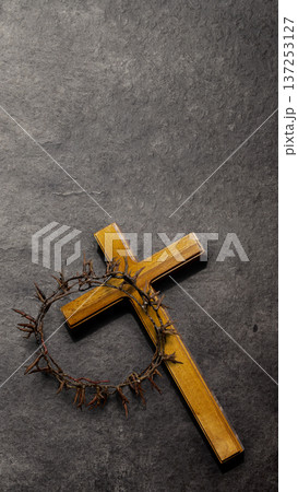 A wooden cross with a crown of thorns resting on it, set against a dark textured slate background. Symbolic of Jesus Christ's sacrifice, Good Friday, and Easter A wooden cross with a crown of thorns resting on it, set against a dark textured slate background. Symbolic of Jesus Christ's sacrifice, Good Friday, and Easter 137253127