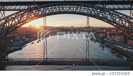 Portugal, Porto: Historic Dom Luis I Bridge framing cityscape skyline at golden hour over Douro River with traditional rabelo boats below. People enjoy colorful sunset. Aerial zoom out drone flight Portugal, Porto: Historic Dom Luis I Bridge framing cityscape skyline at golden hour over Douro River with traditional rabelo boats below. People enjoy colorful sunset. Aerial zoom out drone flight 137253163