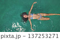 Beautiful woman in blue bikini floating on her back in crystal clear turquoise ocean water, enjoying a relaxing travel vacation and summer holiday recreation. Top down aerial view zoom out Beautiful woman in blue bikini floating on her back in crystal clear turquoise ocean water, enjoying a relaxing travel vacation and summer holiday recreation. Top down aerial view zoom out 137253271