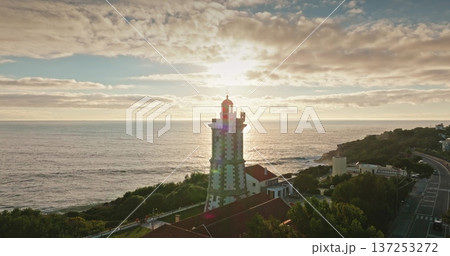 Portugal, Lisbon: Guia Lighthouse standing on the coast, near Cascais, during a beautiful warm light sunset, with sun rays bathing the structure and illuminating the ocean. Aerial drone panorama Portugal, Lisbon: Guia Lighthouse standing on the coast, near Cascais, during a beautiful warm light sunset, with sun rays bathing the structure and illuminating the ocean. Aerial drone panorama 137253272