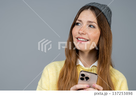 Cute young woman with a phone in hand on a grey background 137253898