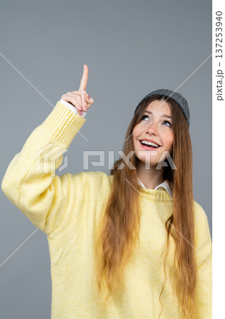 Young woman in yellow sweater pointing up with her finger 137253940