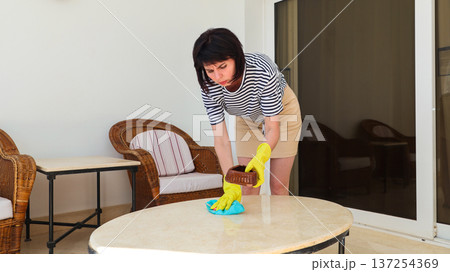 A woman dusts a table on a balcony A woman dusts a table on a balcony 137254369
