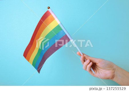 Hand holding rainbow flag on blue background. Hand holding rainbow flag on blue background. 137255529
