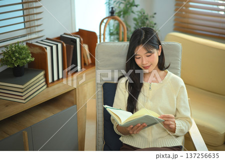 Happy relaxed young woman resting sitting on armchair reading daily and holding coffee cup Happy relaxed young woman resting sitting on armchair reading daily and holding coffee cup 137256635