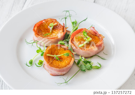 King oyster mushrooms wrapped in crispy bacon served as elegant gourmet appetizer on white plate 137257272