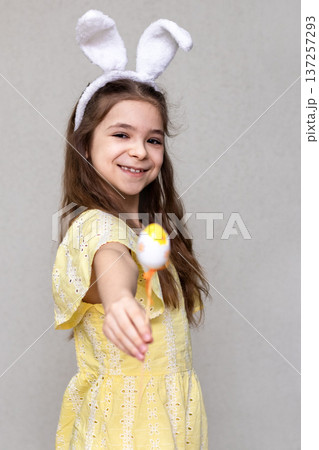 Smiling girl in bunny ears holding a decorated Easter egg while wearing a yellow dress Smiling girl in bunny ears holding a decorated Easter egg while wearing a yellow dress 137257293