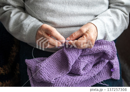 Elderly hands knitting a purple sweater by hand, cozy handmade craft and patient hobby at home 137257308