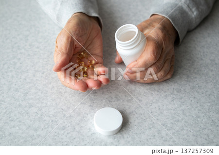 Elderly hands holding vitamin capsules with pill bottle on kitchen table for senior health 137257309