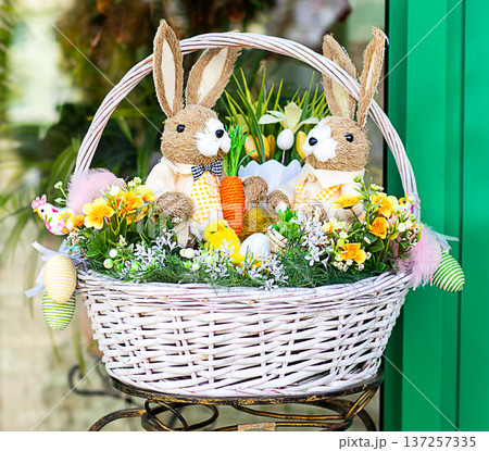 Easter bunny basket with plush rabbit, eggs, flowers and spring decoration for holiday display Easter bunny basket with plush rabbit, eggs, flowers and spring decoration for holiday display 137257335