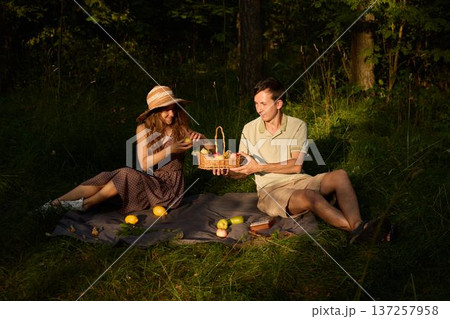 Joyful couple sharing apple beneath dappled sunlight outdoors Joyful couple sharing apple beneath dappled sunlight outdoors 137257958