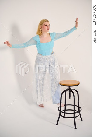 Blonde woman in pale blue outfit balances delicately beside stool Blonde woman in pale blue outfit balances delicately beside stool 137257970