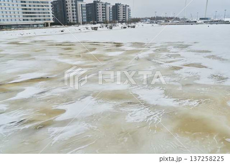 Cold city shoreline scene. Snowy waterfront with thin ice patches Cold city shoreline scene. Snowy waterfront with thin ice patches 137258225