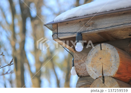 Cozy wooden log cabin corner decorated with light bulbs and covered in fresh white snow in winter. 137259559