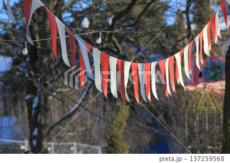 Red and white festive bunting flags hanging on a string in a sunny park during a winter celebration. Red and white festive bunting flags hanging on a string in a sunny park during a winter celebration. 137259568