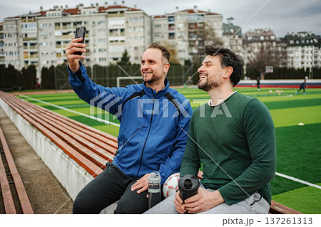 Adult men friends sitting on stadium bench taking selfie enjoying sport 137261313