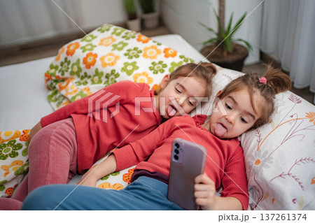 Twin girls making funny faces taking smartphone selfie Twin girls making funny faces taking smartphone selfie 137261374