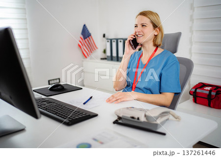 Healthcare professional talking on phone at desk with American flag 137261446