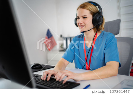 Nurse wearing headset typing on computer for telehealth consultation Nurse wearing headset typing on computer for telehealth consultation 137261447