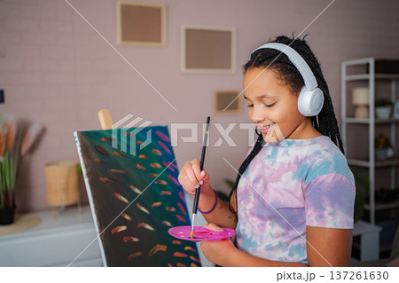 Girl wearing headphones painting on canvas at home 137261630