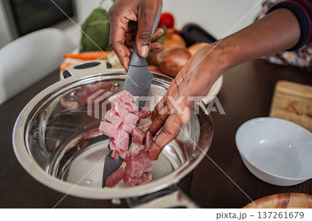 Adult hands transferring diced raw meat into a cooking pot 137261679