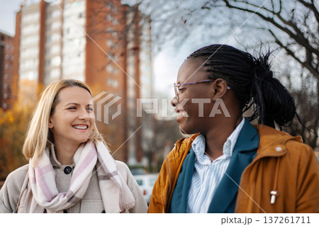Two diverse adult women friends smiling and talking outdoors Two diverse adult women friends smiling and talking outdoors 137261711