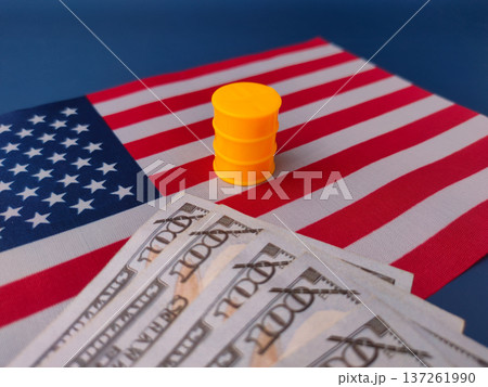 The image illustrates the relationship between the US dollar currency and the oil industry, featuring cash on a US flag with a miniature oil barrel. 137261990