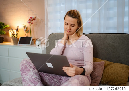 Woman working on laptop experiencing neck pain in bed Woman working on laptop experiencing neck pain in bed 137262013