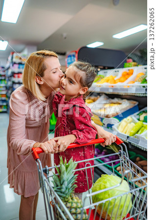 Mother kissing daughter in supermarket while grocery shopping Mother kissing daughter in supermarket while grocery shopping 137262065