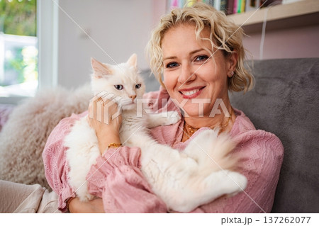 Woman holding fluffy white cat smiling at home Woman holding fluffy white cat smiling at home 137262077