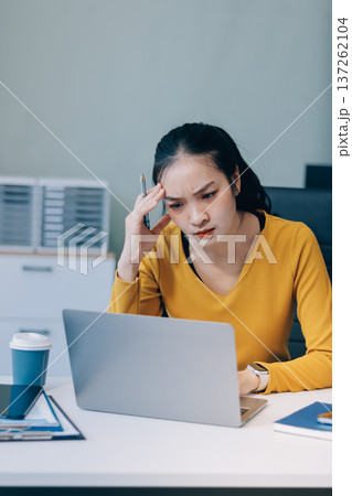 Young professional woman suffering from headache while analyzing financial charts and graphs on computer, experiencing work related stress in modern office Young professional woman suffering from headache while analyzing financial charts and graphs on computer, experiencing work related stress in modern office 137262104