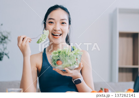Fit young Asian women in activewear sitting on yoga mat and eating fresh vegetable salad after workout, representing clean eating, fitness lifestyle, wellness routine and health balance. Fit young Asian women in activewear sitting on yoga mat and eating fresh vegetable salad after workout, representing clean eating, fitness lifestyle, wellness routine and health balance. 137262141