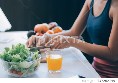 Fit young Asian women in activewear sitting on yoga mat and eating fresh vegetable salad after workout, representing clean eating, fitness lifestyle, wellness routine and health balance. 137262149