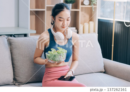 Fit young Asian women in activewear sitting on yoga mat and eating fresh vegetable salad after workout, representing clean eating, fitness lifestyle, wellness routine and health balance. Fit young Asian women in activewear sitting on yoga mat and eating fresh vegetable salad after workout, representing clean eating, fitness lifestyle, wellness routine and health balance. 137262161