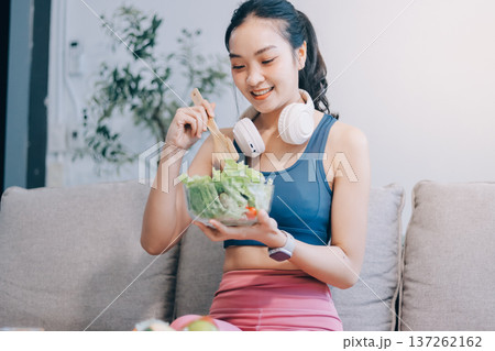 Fit young Asian women in activewear sitting on yoga mat and eating fresh vegetable salad after workout, representing clean eating, fitness lifestyle, wellness routine and health balance. Fit young Asian women in activewear sitting on yoga mat and eating fresh vegetable salad after workout, representing clean eating, fitness lifestyle, wellness routine and health balance. 137262162