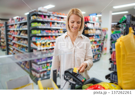 Woman paying for groceries using contactless credit card terminal Woman paying for groceries using contactless credit card terminal 137262261