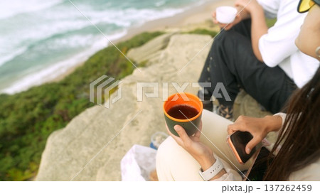 Group sharing warm drinks overlooking rocky coast and sea view 137262459